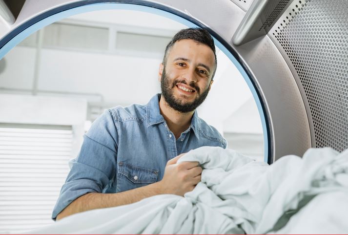 Mann holt Wäsche aus einer Waschmaschine